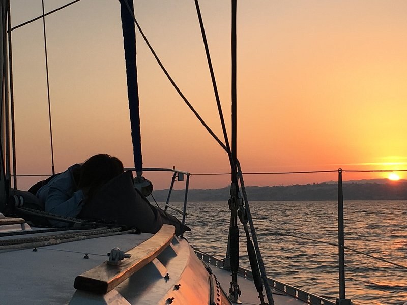 A sailboat's bow rail and rigging against an orange sunset