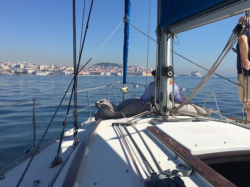 A sailboat's foredeck in sunshine with the city spread along the far bank