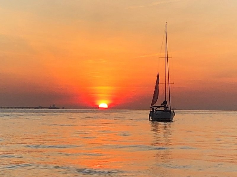 A lone sailboat on the river as the sun goes down