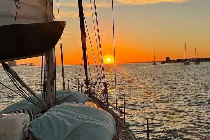 A sailboat's cockpit and boom as the sun sets over the river