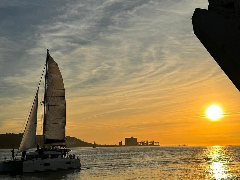 A sailing catamaran in silhouette against a low evening sun