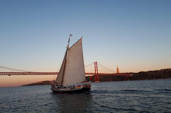 A traditional river boat under a gaff sail, with the bridge behind it